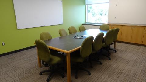 Room with one rectangular table, 10 office chairs, white board on wall, with window