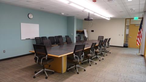 Room with large rectangular table, 20 office chairs, white board on the wall