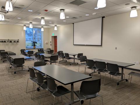 Large room with tables and chairs set up classroom style, projector screen on wall